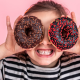 Niña con dos donuts de chocolate, lo cual provoca caries infantil
